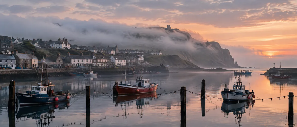 GPT Image 2.5 ultra-wide 21:9 panorama of a small harbour town at first light with fishing boats on glassy water